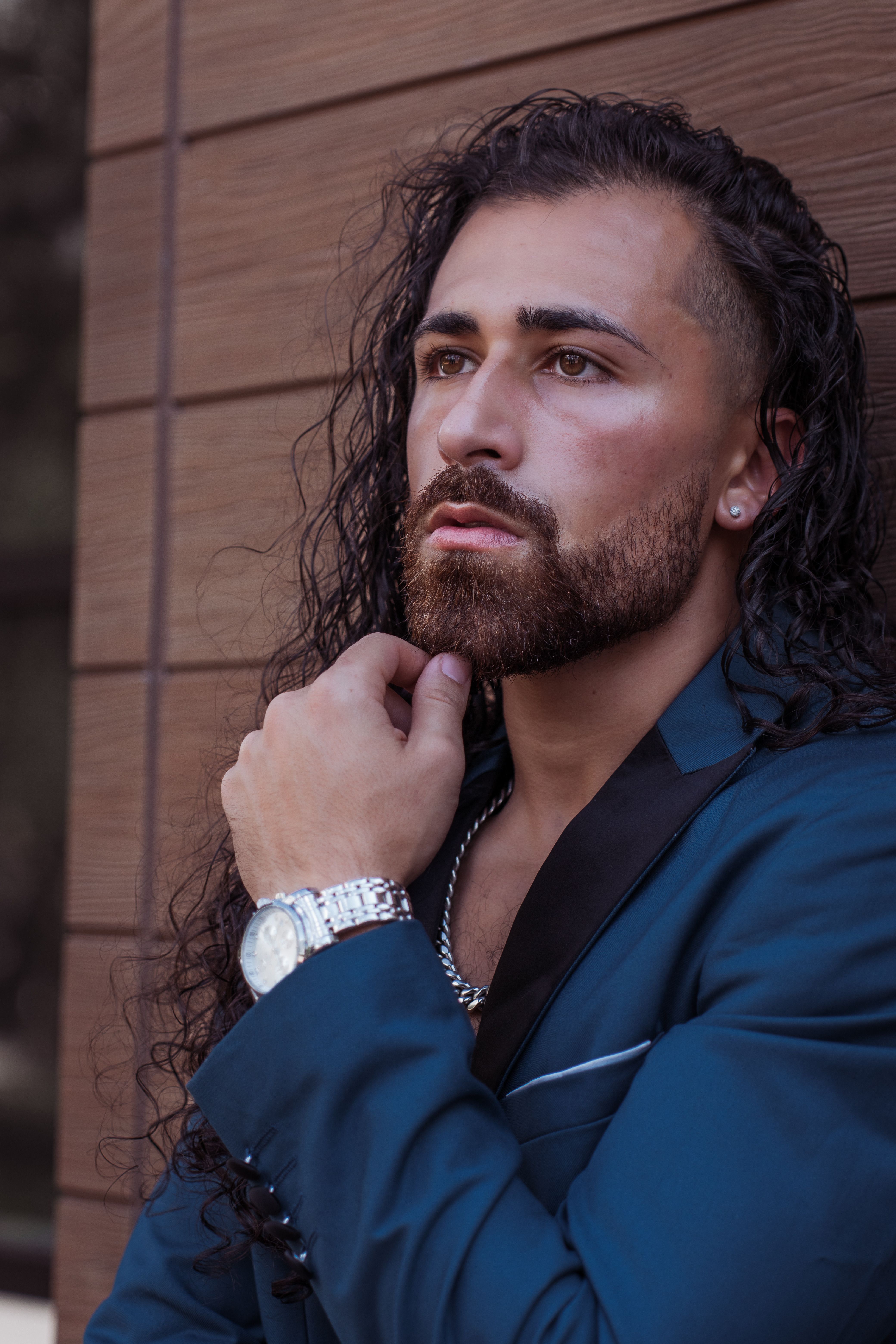 Portrait of a contemplative man with long hair in a blue suit, showcasing modern fashion style.