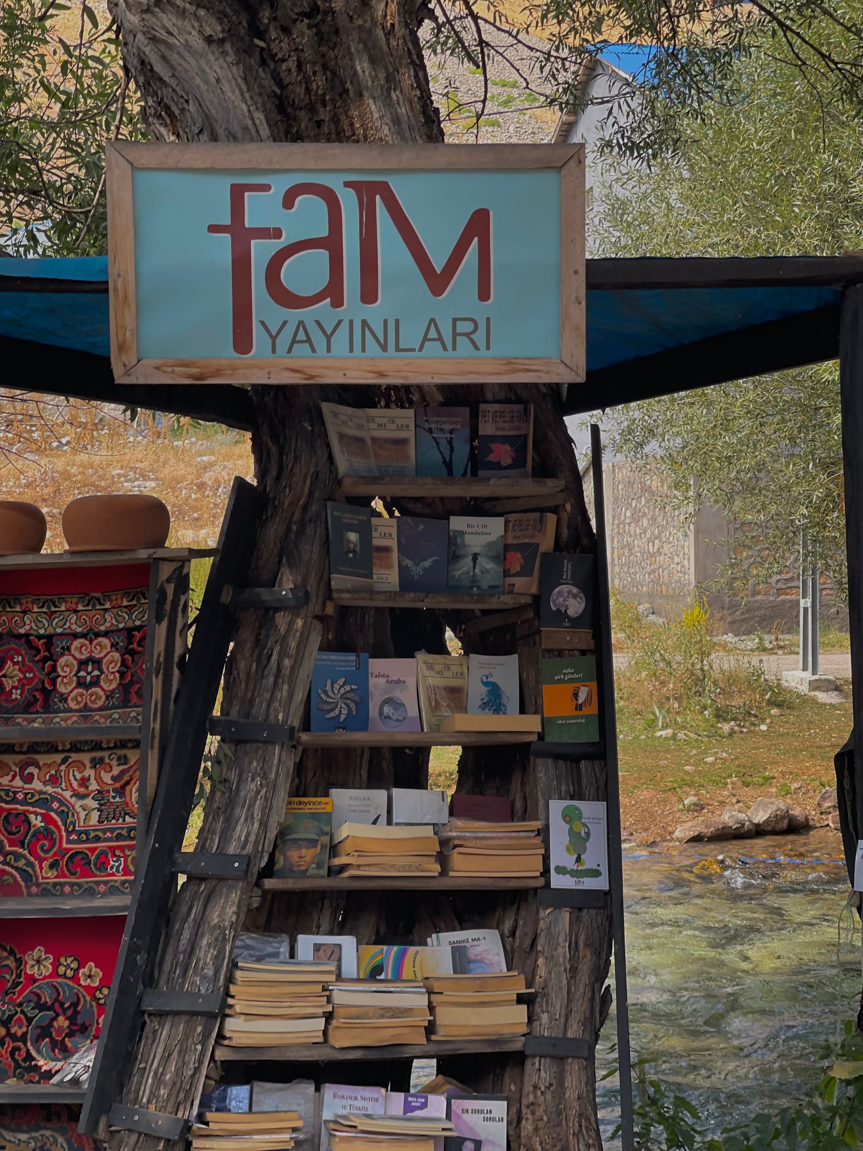 Rustic outdoor book display in Tunceli, Türkiye, featuring a wooden shelf integrated into a tree.