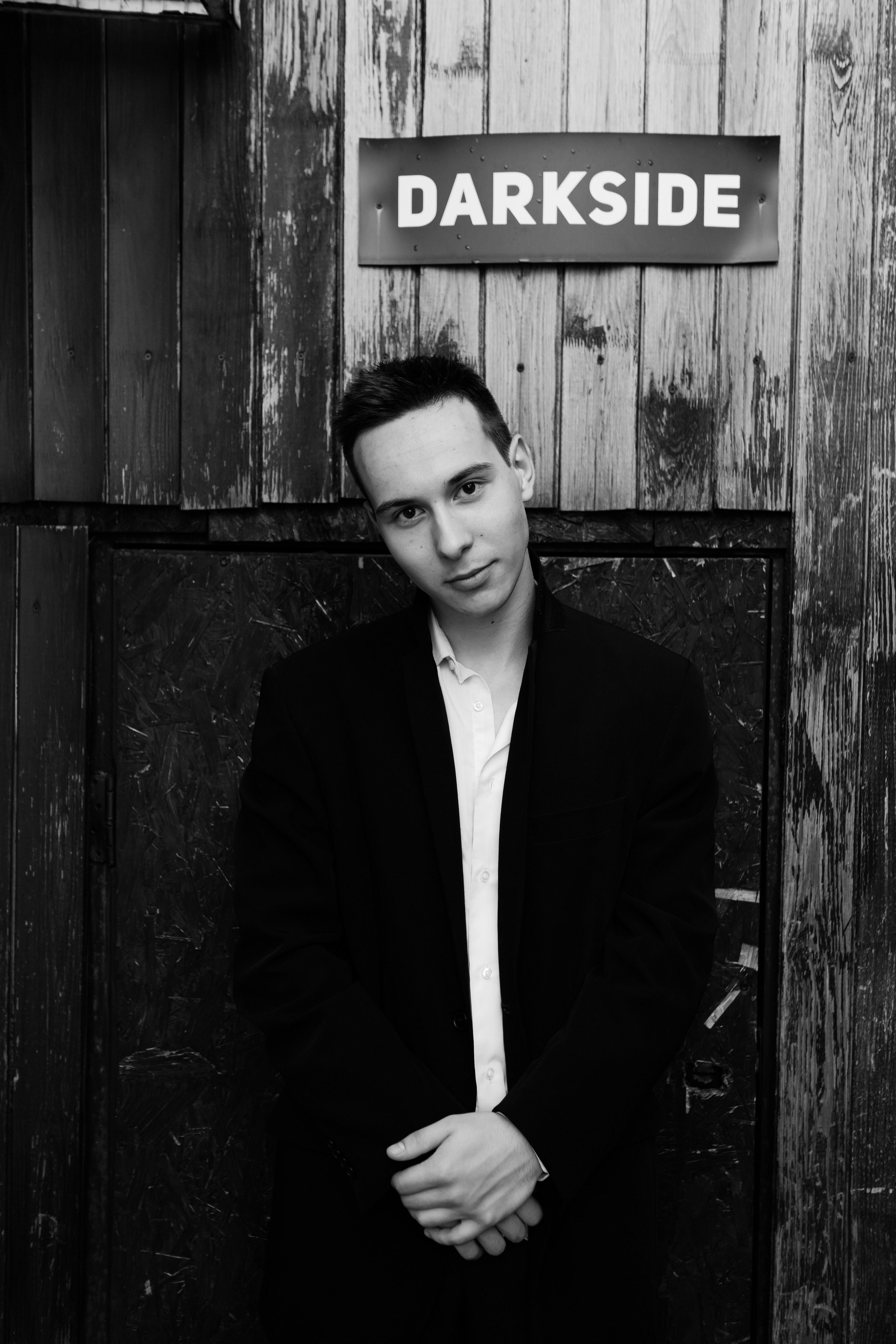 Black and white portrait of a man posing by wooden panels with 'Darkside' sign.