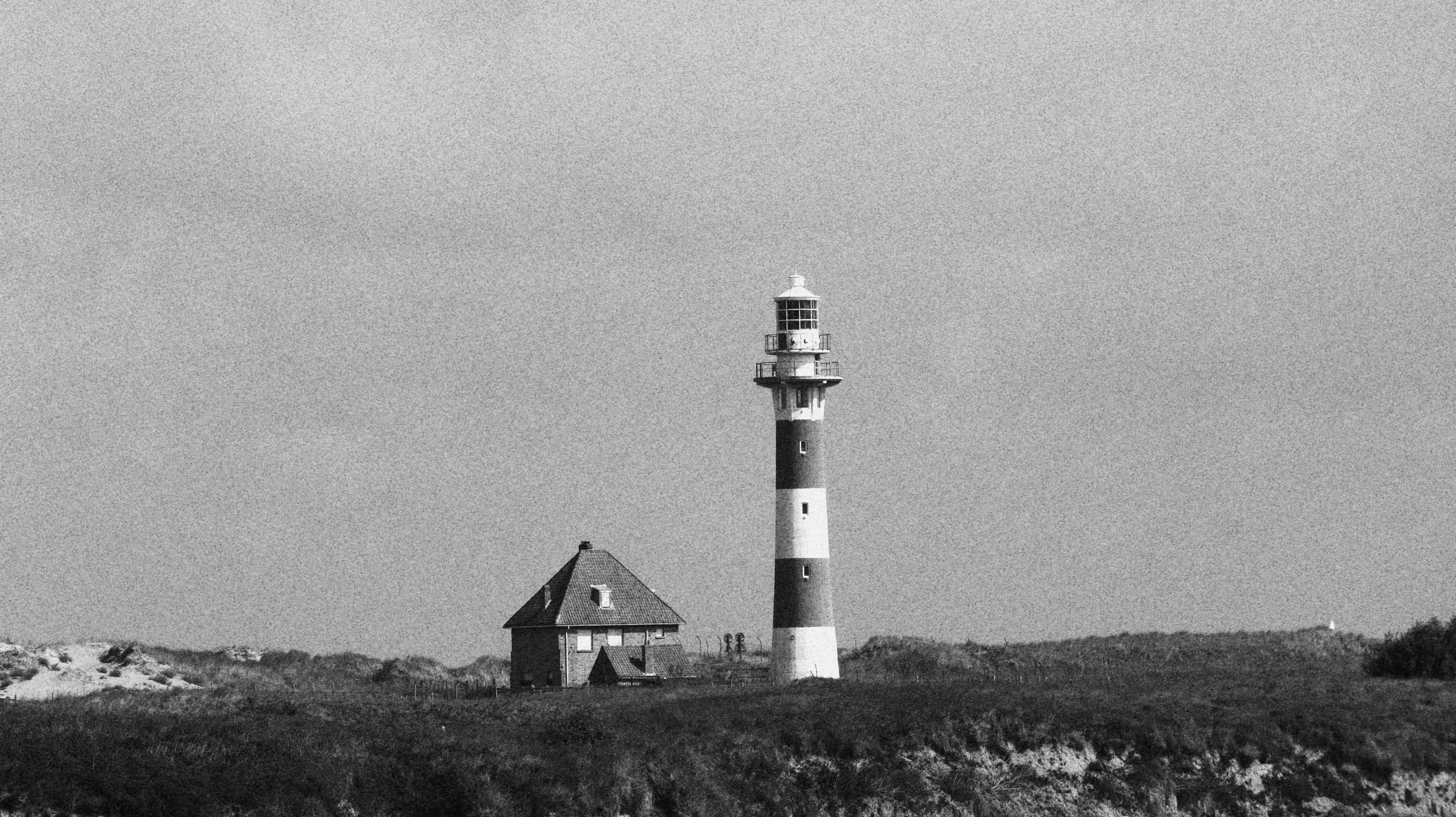 Serene black and white photo of a lighthouse on a coastal hill, radiating calmness.