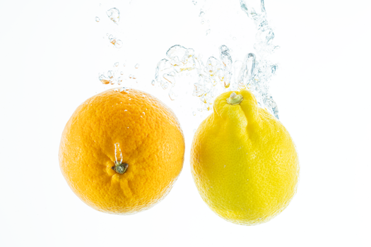 Orange and lemon splash into water, showcasing freshness and vitality on a white backdrop.