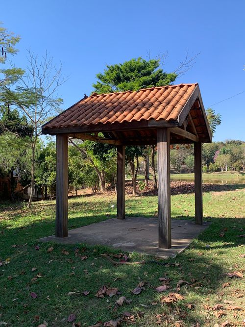 Free A charming wooden gazebo with a tiled roof in a sunny park with lush green trees. Stock Photo