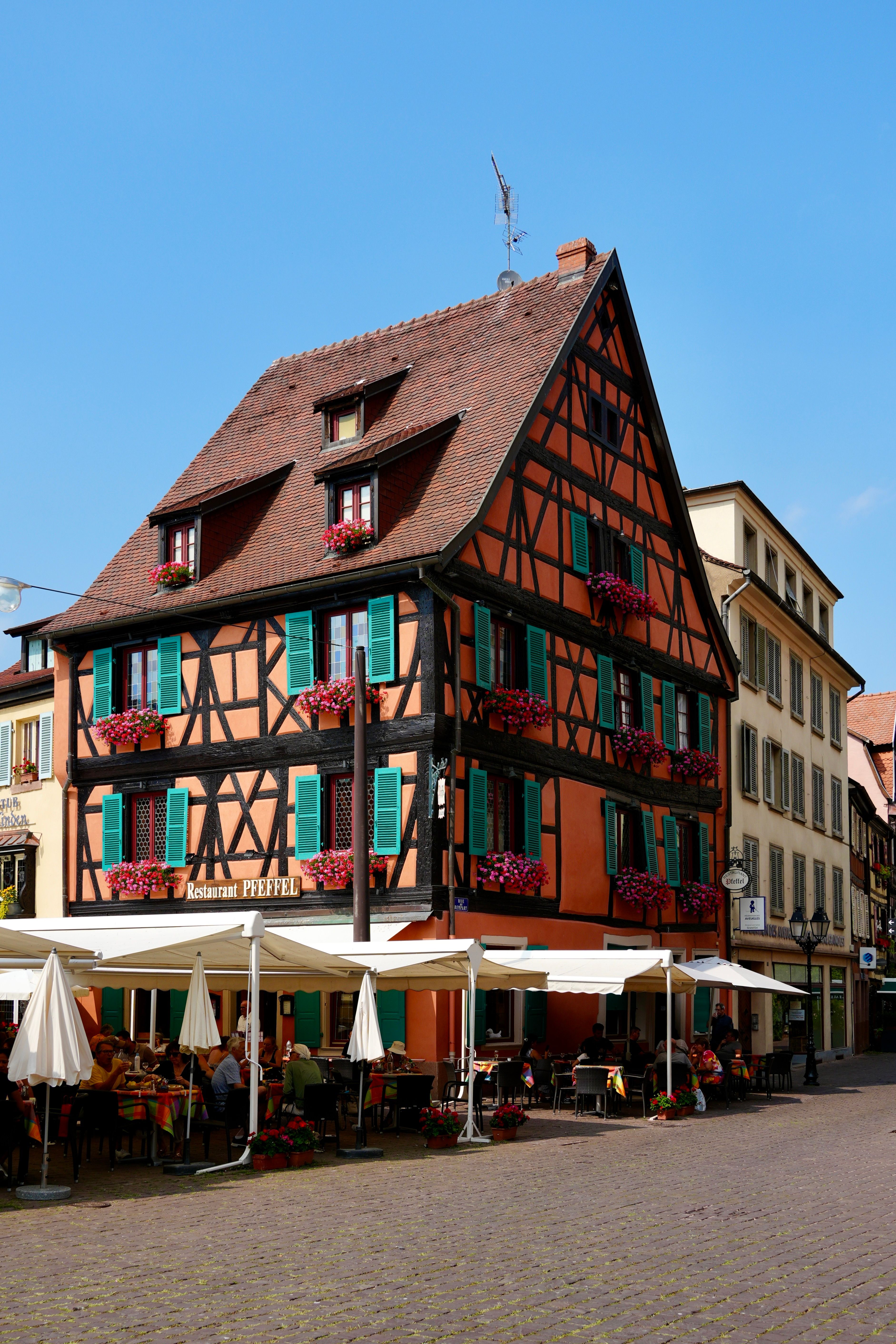 Traditional half-timbered house in Colmar's old town, with vibrant flowers and outdoor cafe seating.