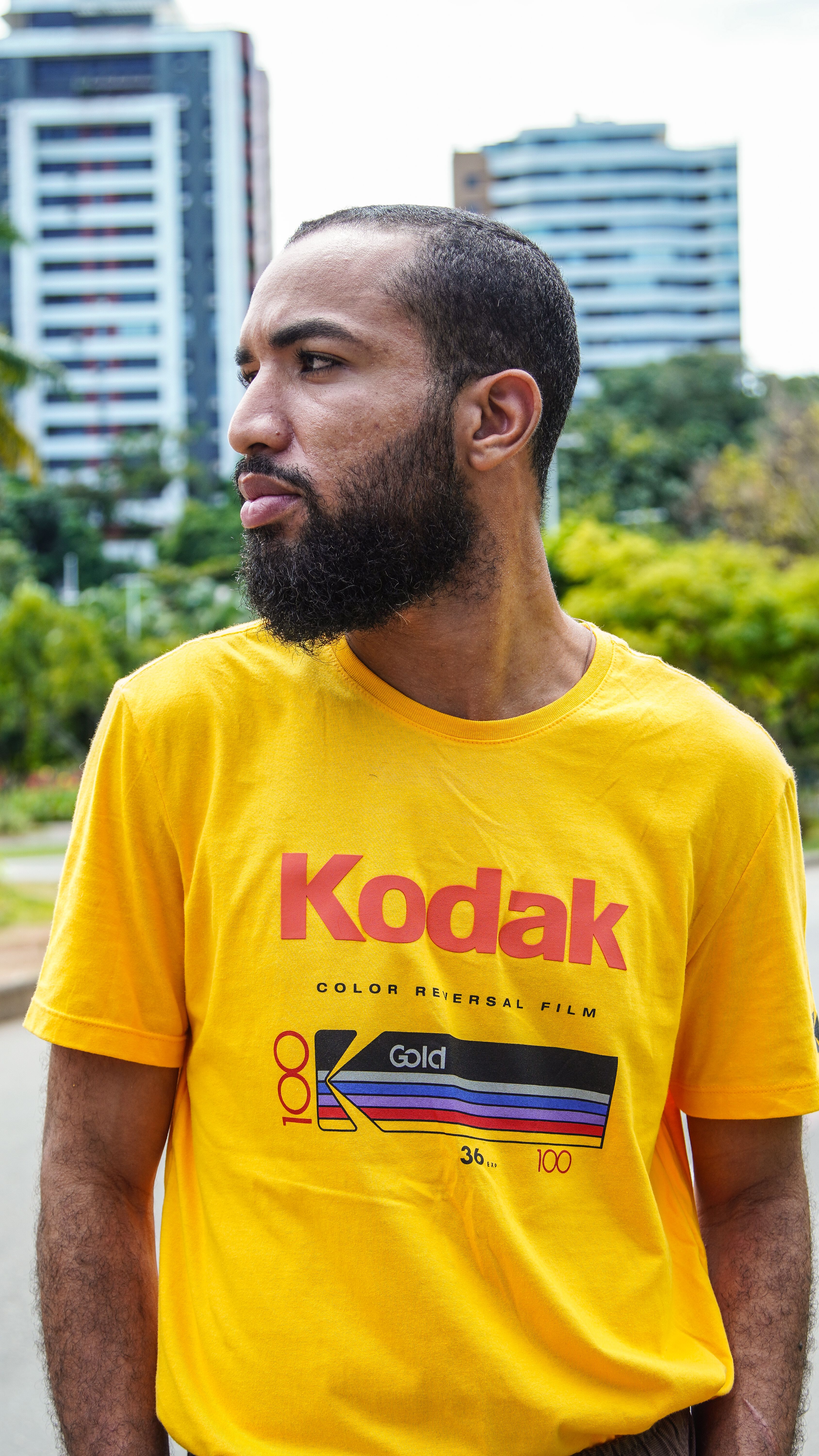 Bearded man wearing a yellow Kodak shirt strolls through a lively outdoor setting in Bahia, Brazil.