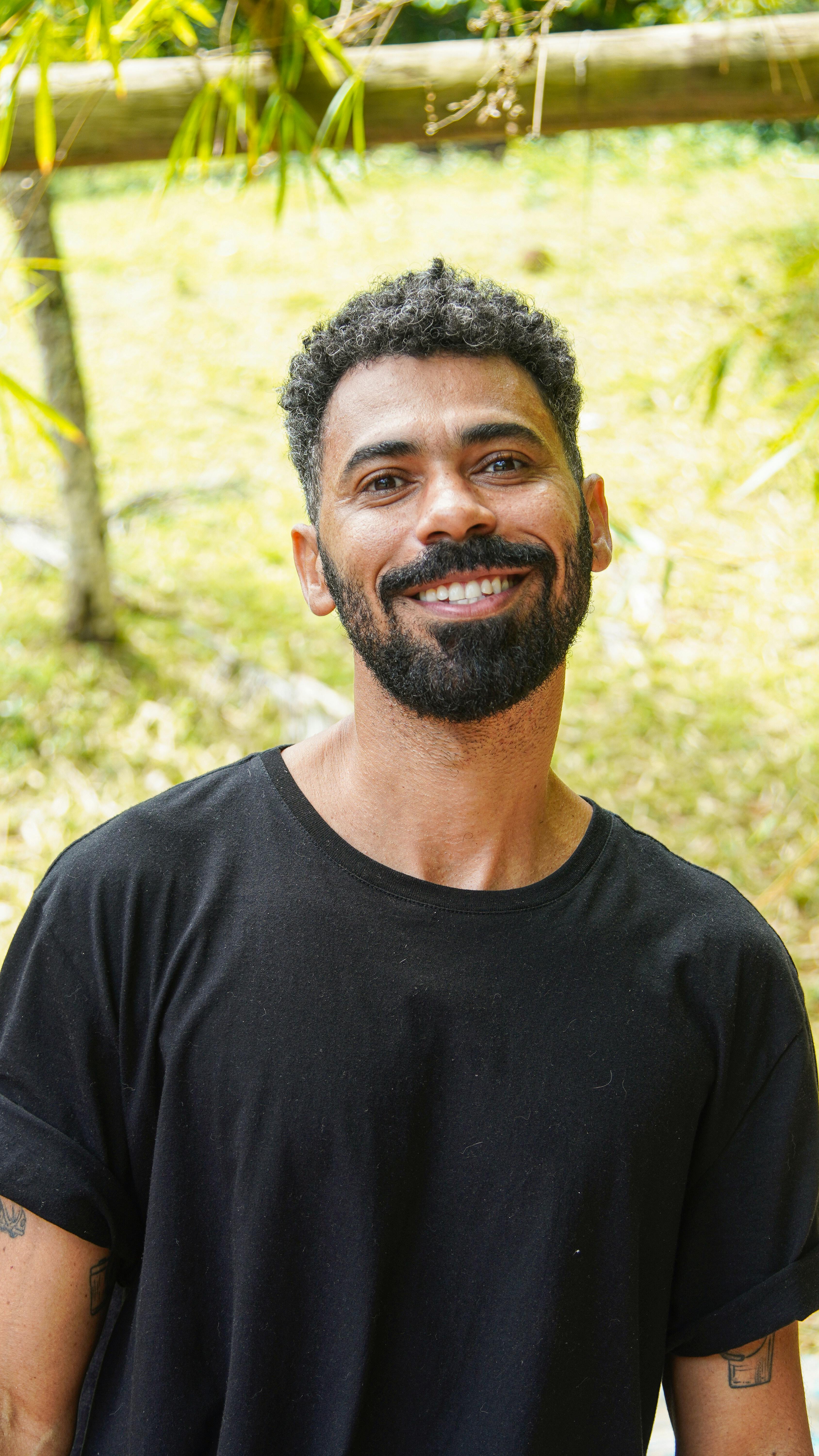 Portrait of a smiling man standing outdoors in Bahia, Brazil, with a natural backdrop.