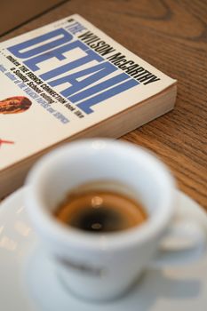 A close-up of an espresso and a book on a wooden table, perfect for a coffee break.
