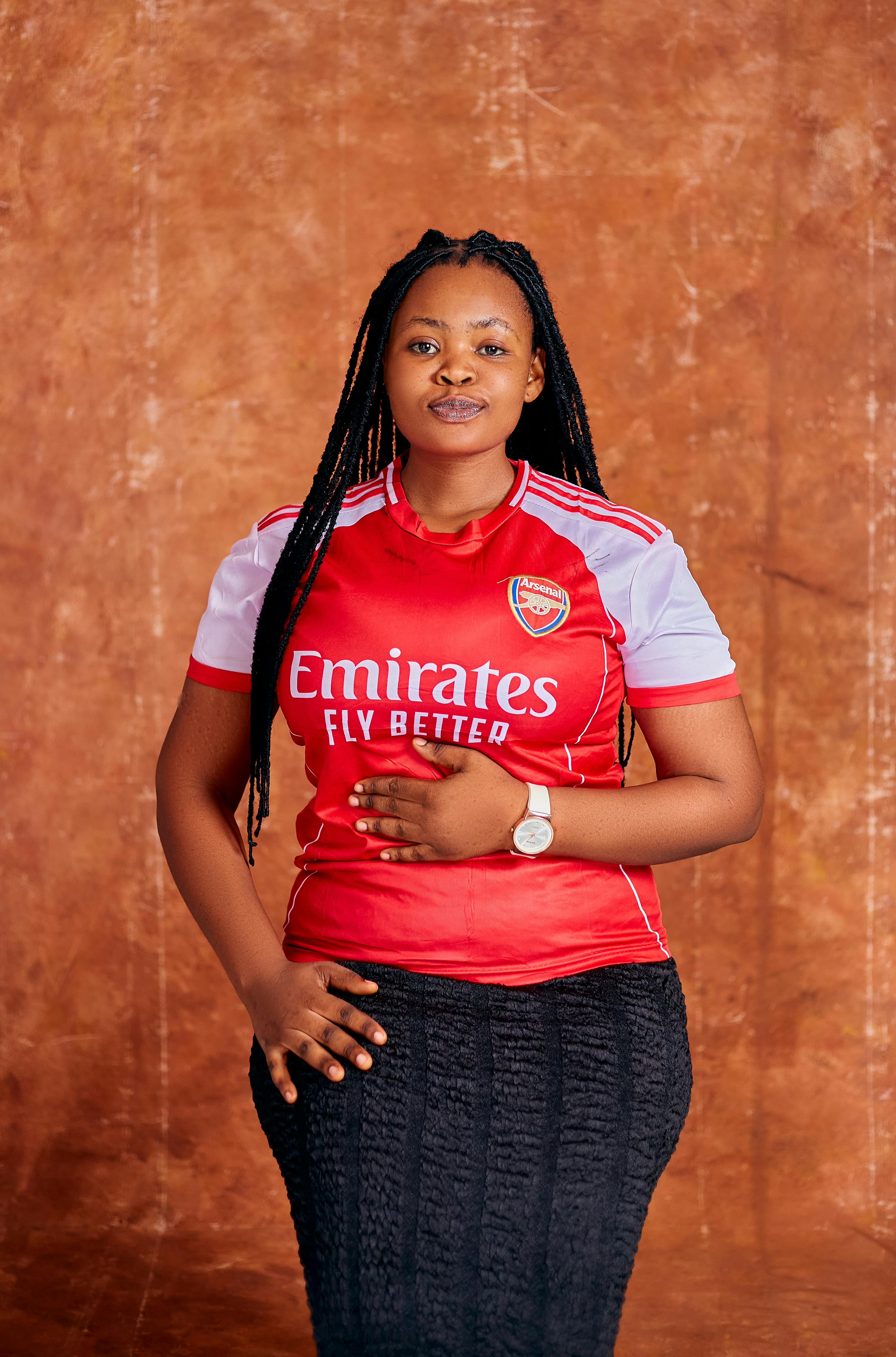 Confident woman posing in red Arsenal jersey against a textured backdrop.