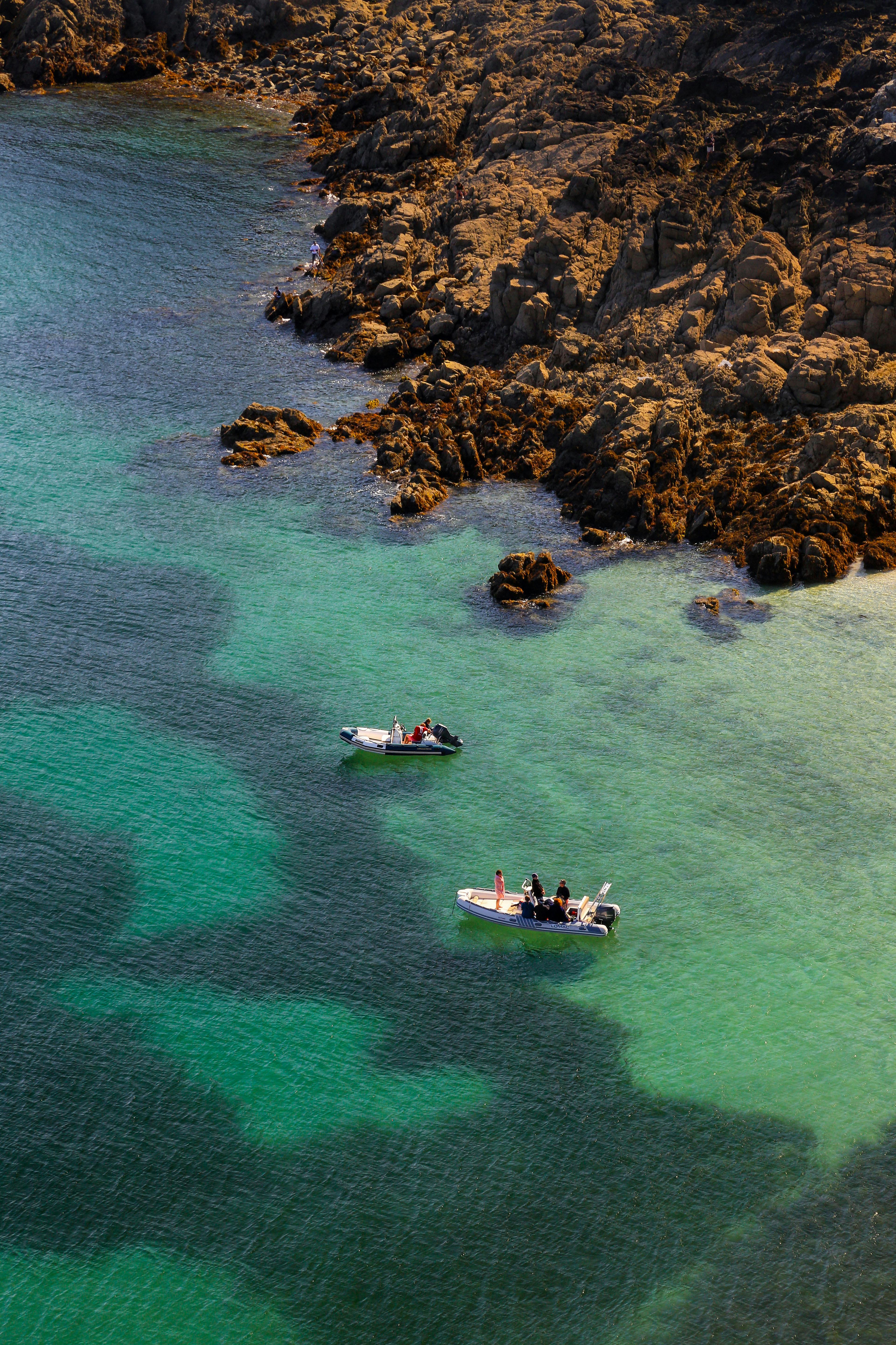 Stunning aerial view of small boats navigating the rocky Bretagne coastline in France under clear skies.
