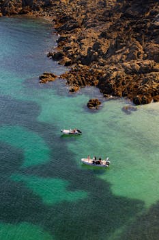 Stunning aerial view of small boats navigating the rocky Bretagne coastline in France under clear skies.