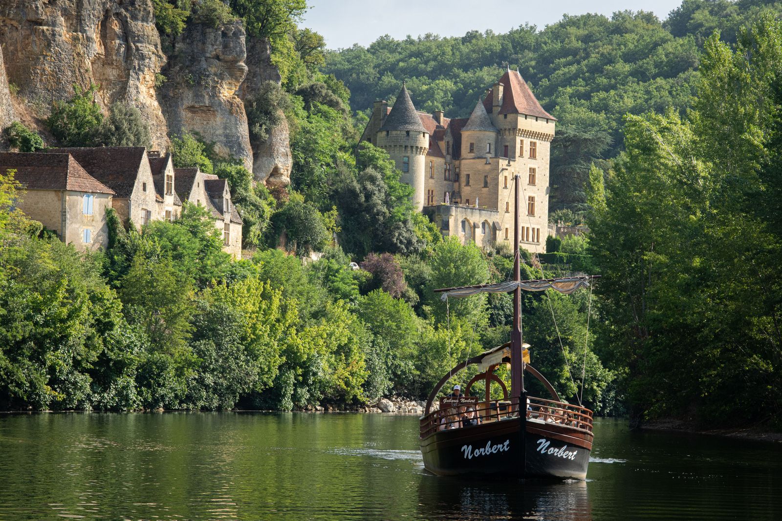 A wooden gabarre on the green Dordogne below the château and cliffs of La Roque-Gageac