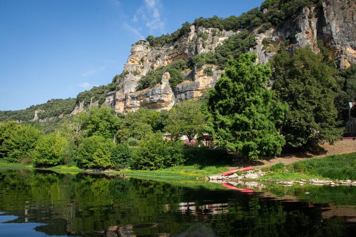 A canoe on the green Dordogne beneath golden limestone cliffs