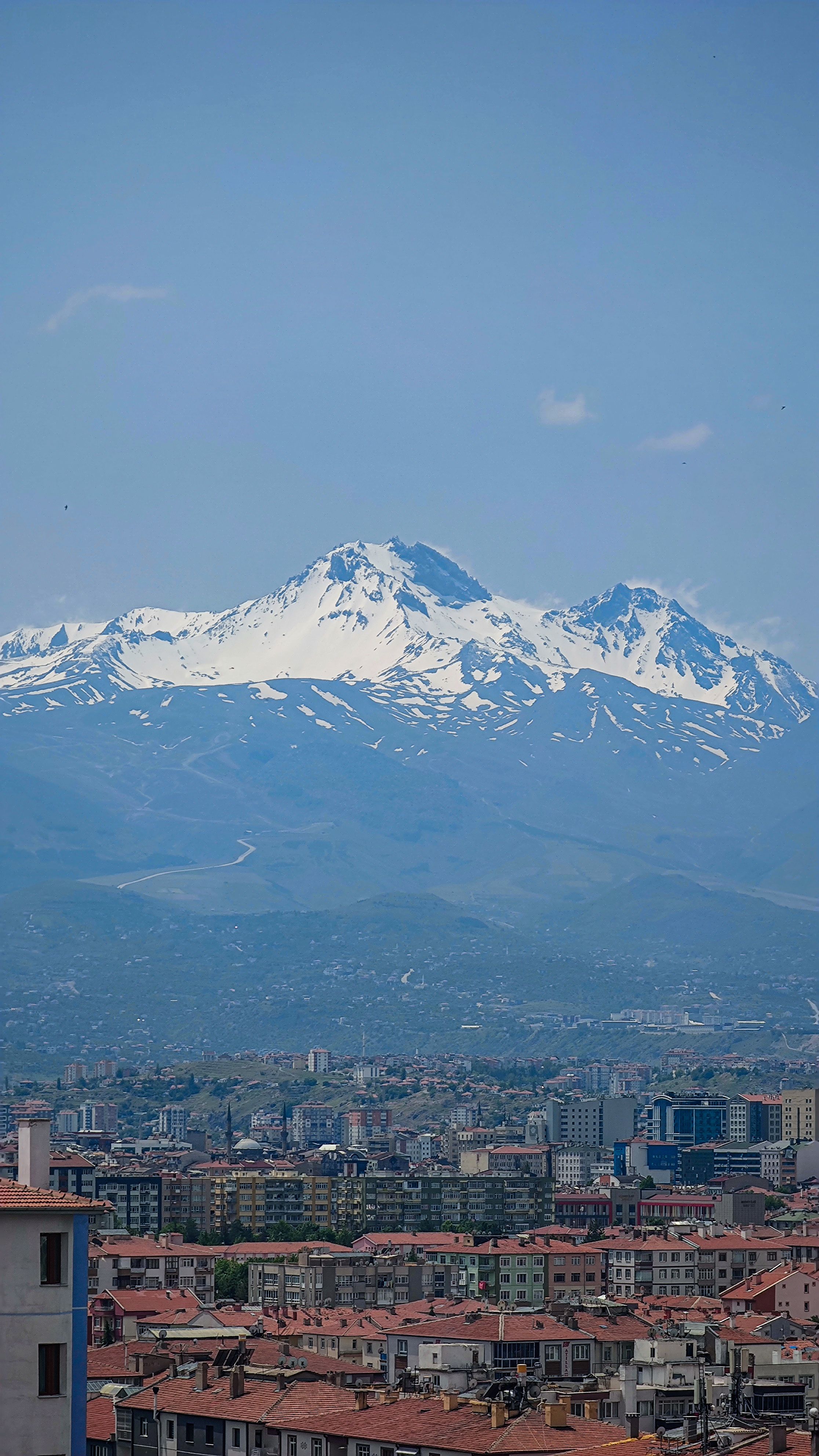 A breathtaking scene of Erciyes mountain over a bustling cityscape under a clear blue sky.