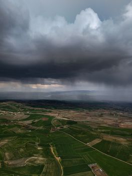 Aerial view of dark clouds and storm over lush green farmland, capturing dramatic weather contrast.