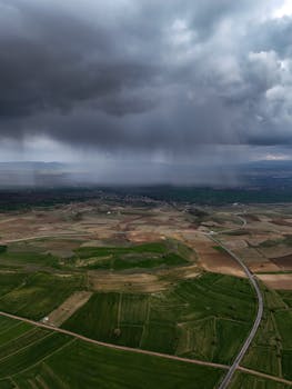 A mesmerizing aerial view of rain clouds looming over sprawling fields, capturing nature's dynamic mood.