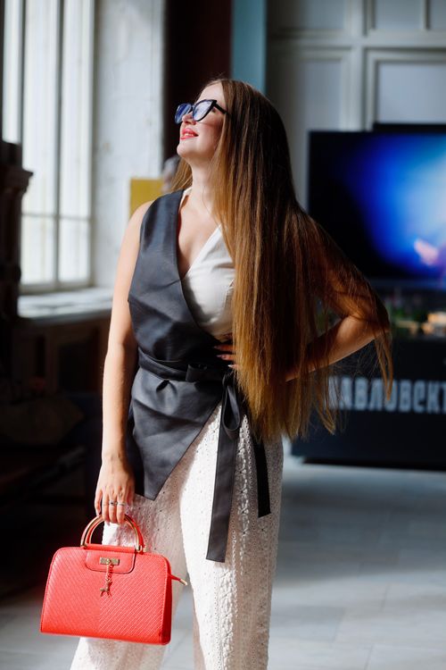 Free Fashionable woman in stylish outfit holding red handbag indoors, looking confident under natural light. Stock Photo