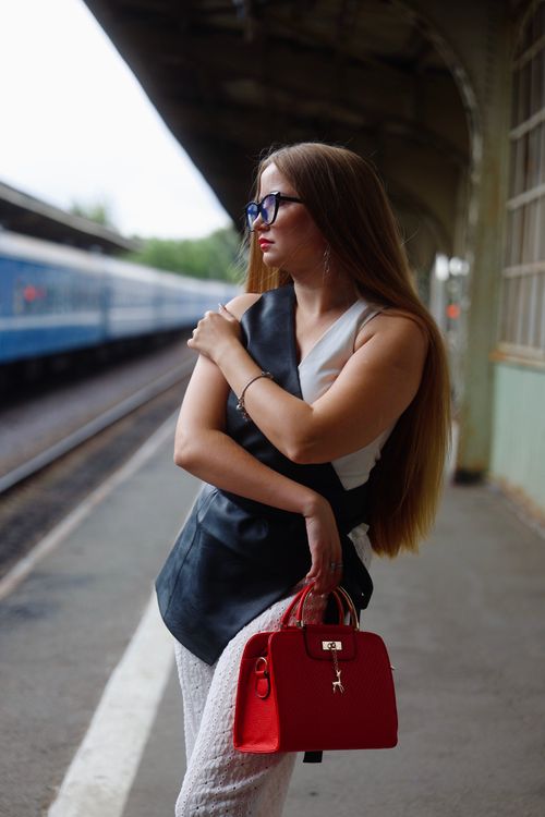 Free Stylish woman at a train station with a red handbag, embodying travel elegance. Stock Photo