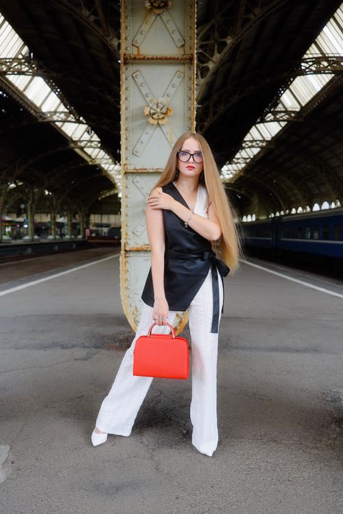 Free Fashionable woman in black and white attire with a red handbag at a vintage train station. Stock Photo