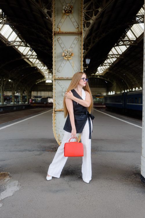 Free Stylish woman posing at an architectural train station with a red handbag. Stock Photo