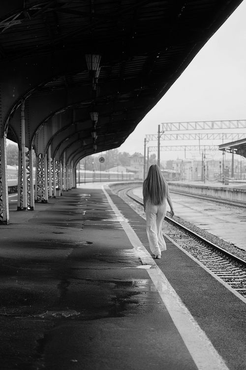 Free A woman walks alone on a deserted train platform, creating a moody and timeless scene. Stock Photo