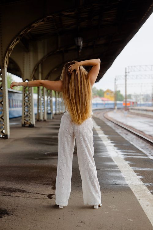 Free Young woman in white clothes standing at an outdoor train station platform. Stock Photo