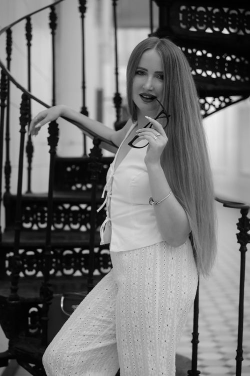 Free Stylish woman posing with glasses on an elegant black spiral staircase indoors. Stock Photo