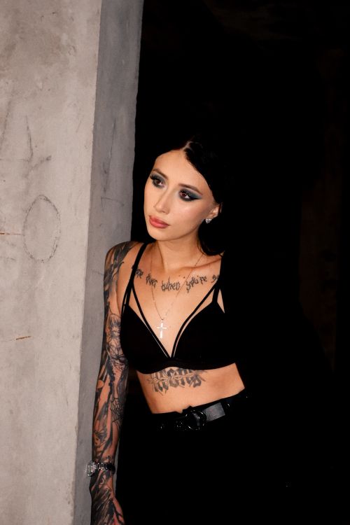 Free Stylish woman with tattoos in black outfit posing indoors against a dark backdrop. Stock Photo