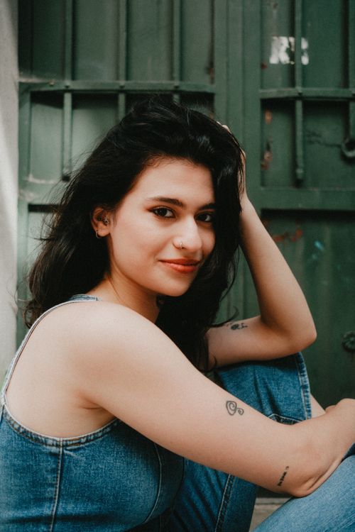 Free Portrait of a young woman sitting casually in denim against a rustic green backdrop. Stock Photo