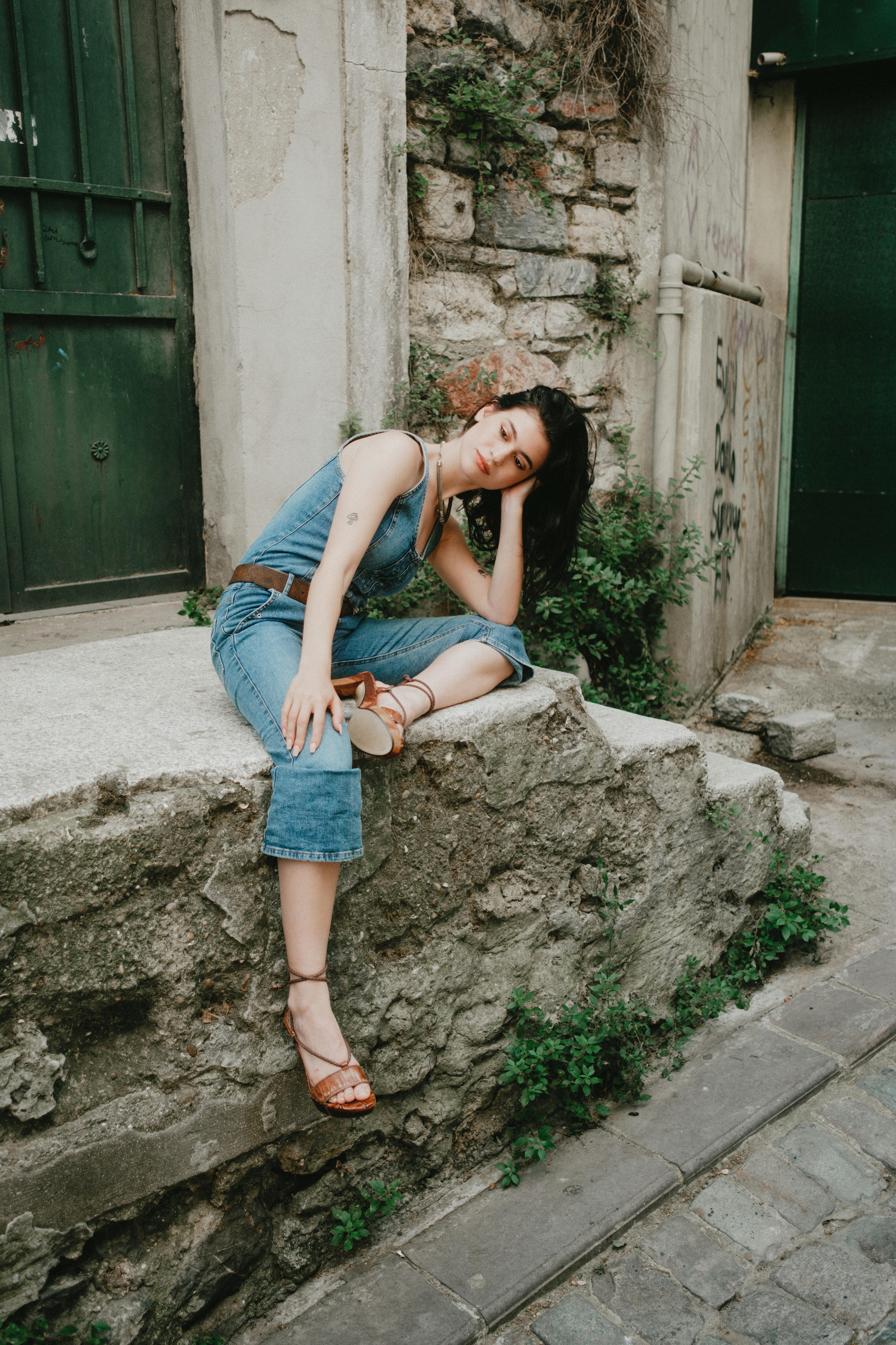 Woman in denim outfit relaxing on a stone bench, serene street setting.