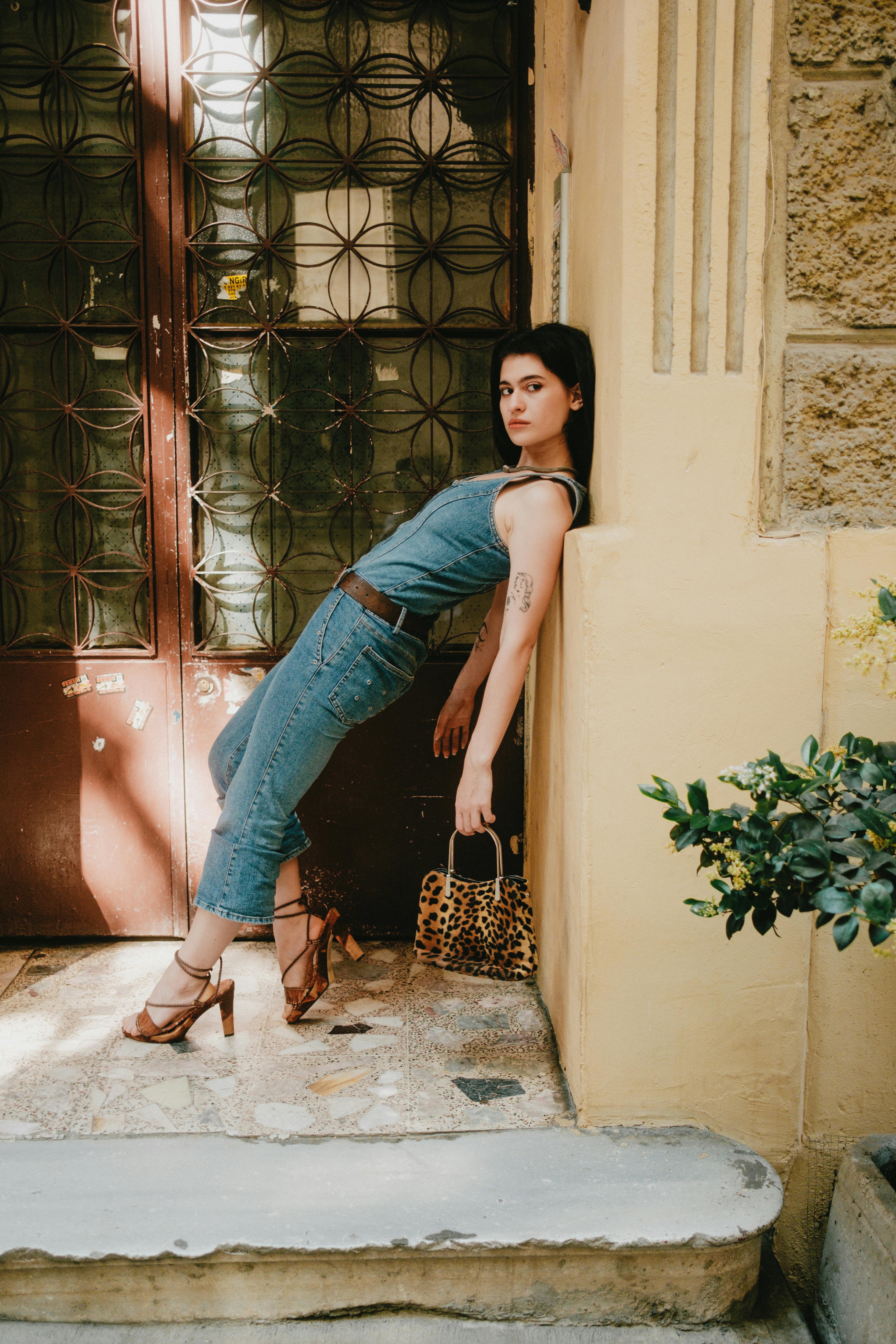 Woman in denim outfit and heels artistically posed against a vintage door.