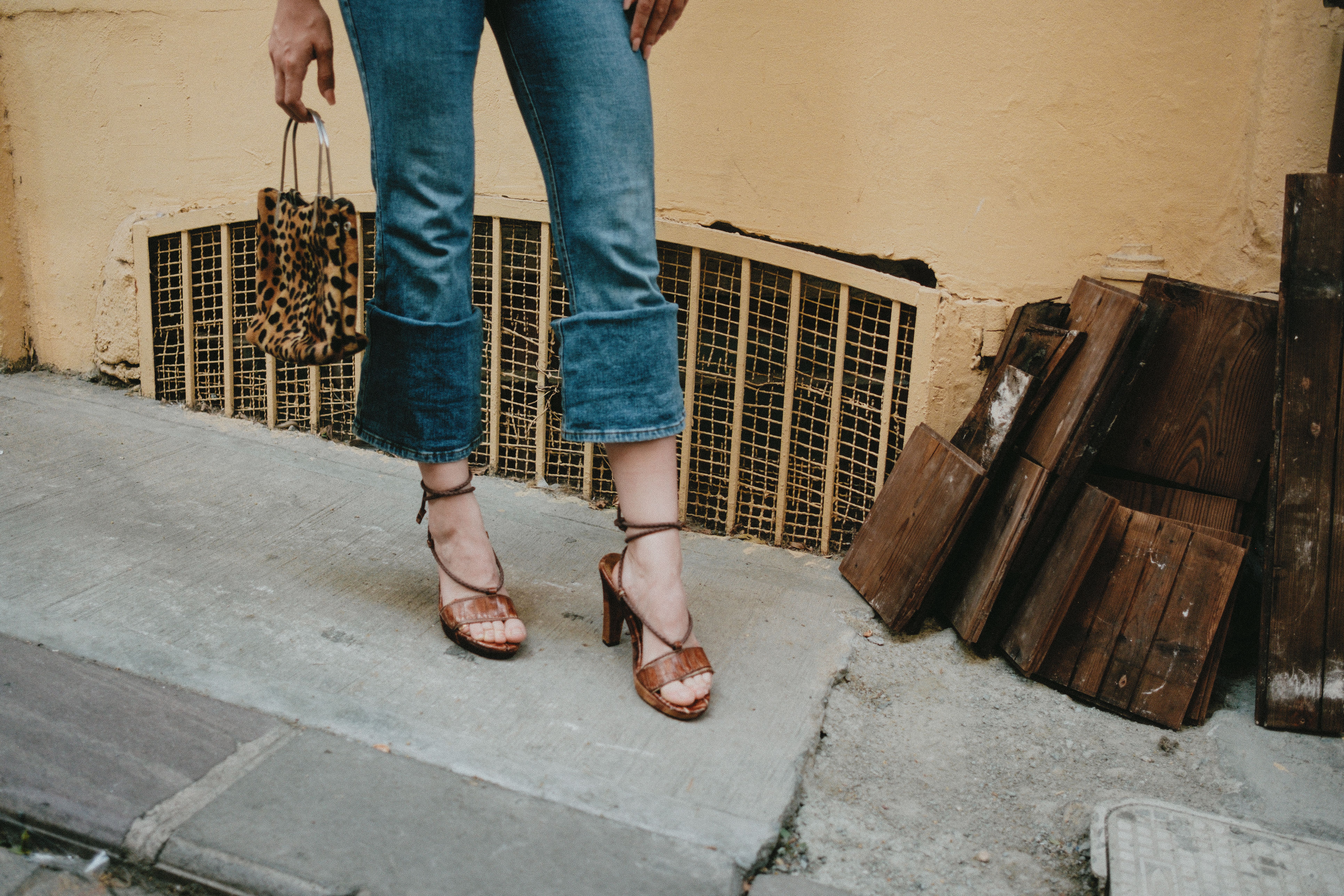 Stylish woman in jeans holding a leopard print bag on city street.