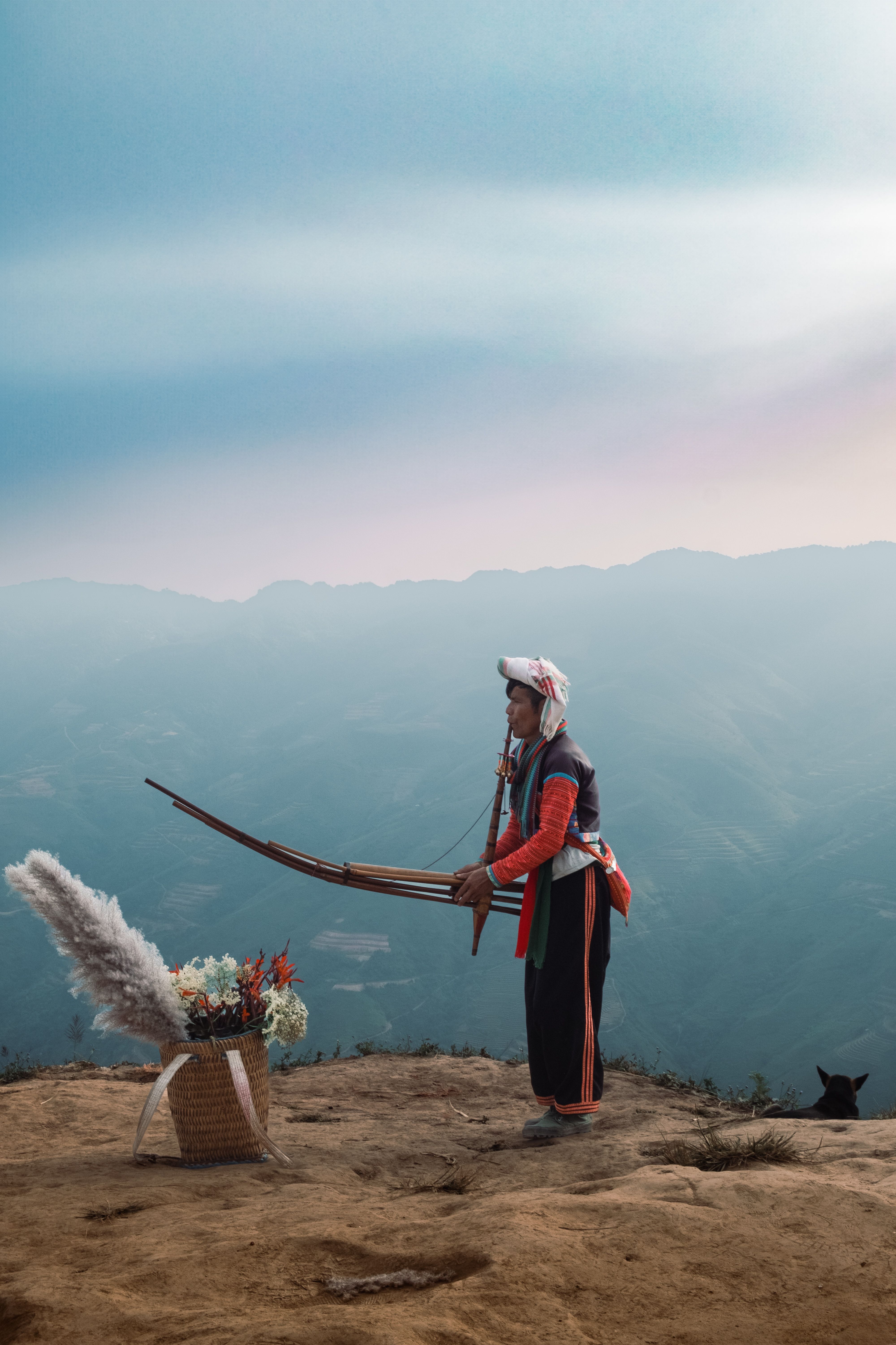 Traditional musician plays an instrument atop a scenic mountain with a beautiful bouquet nearby.