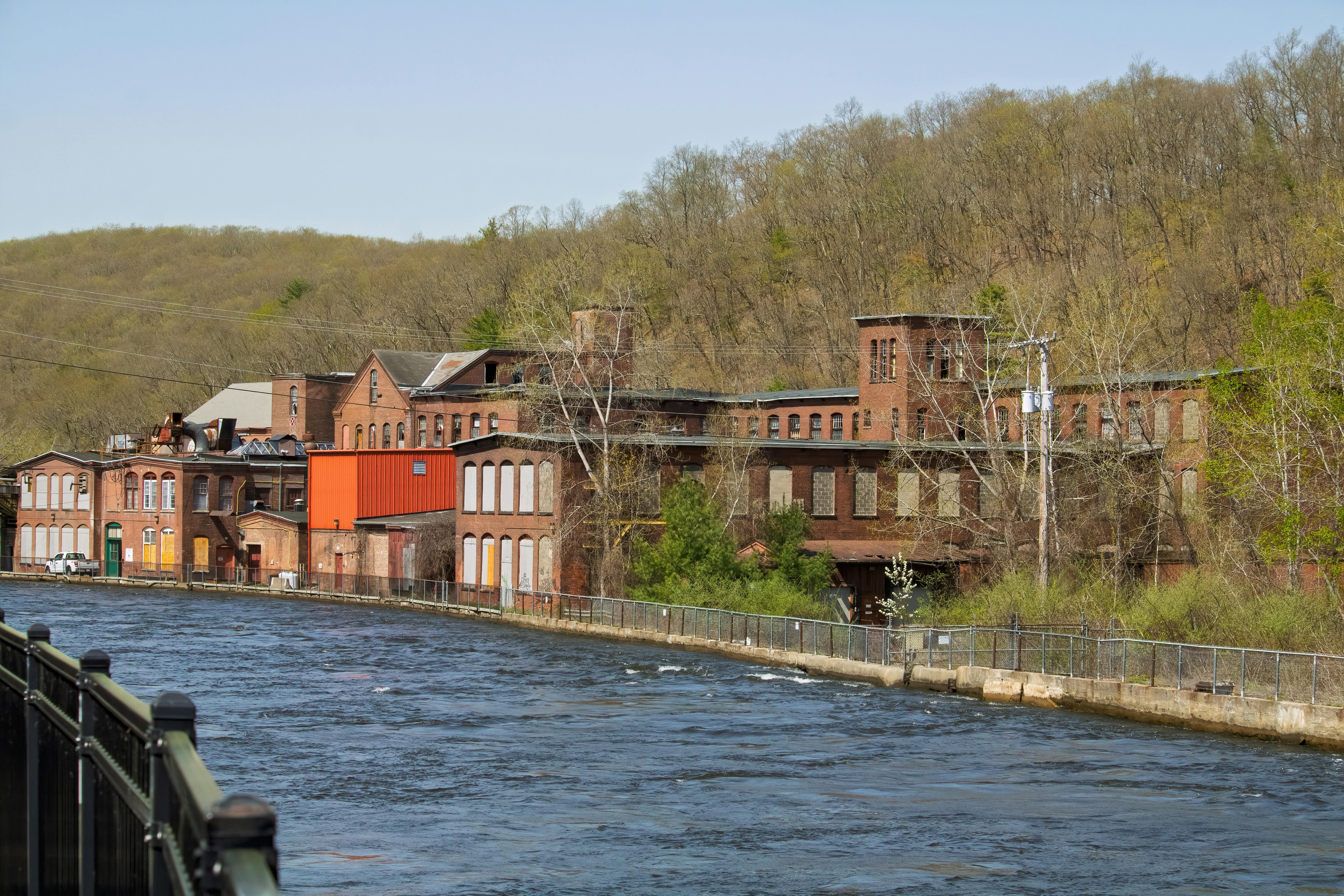 Charming old brick factory by a river in springtime, surrounded by lush greenery.