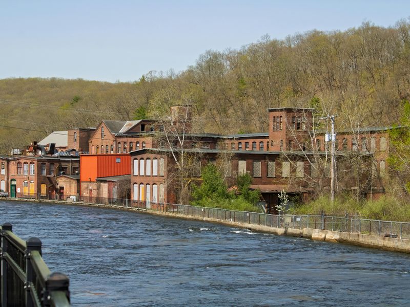 Old brick mill building beside a river amid spring greenery