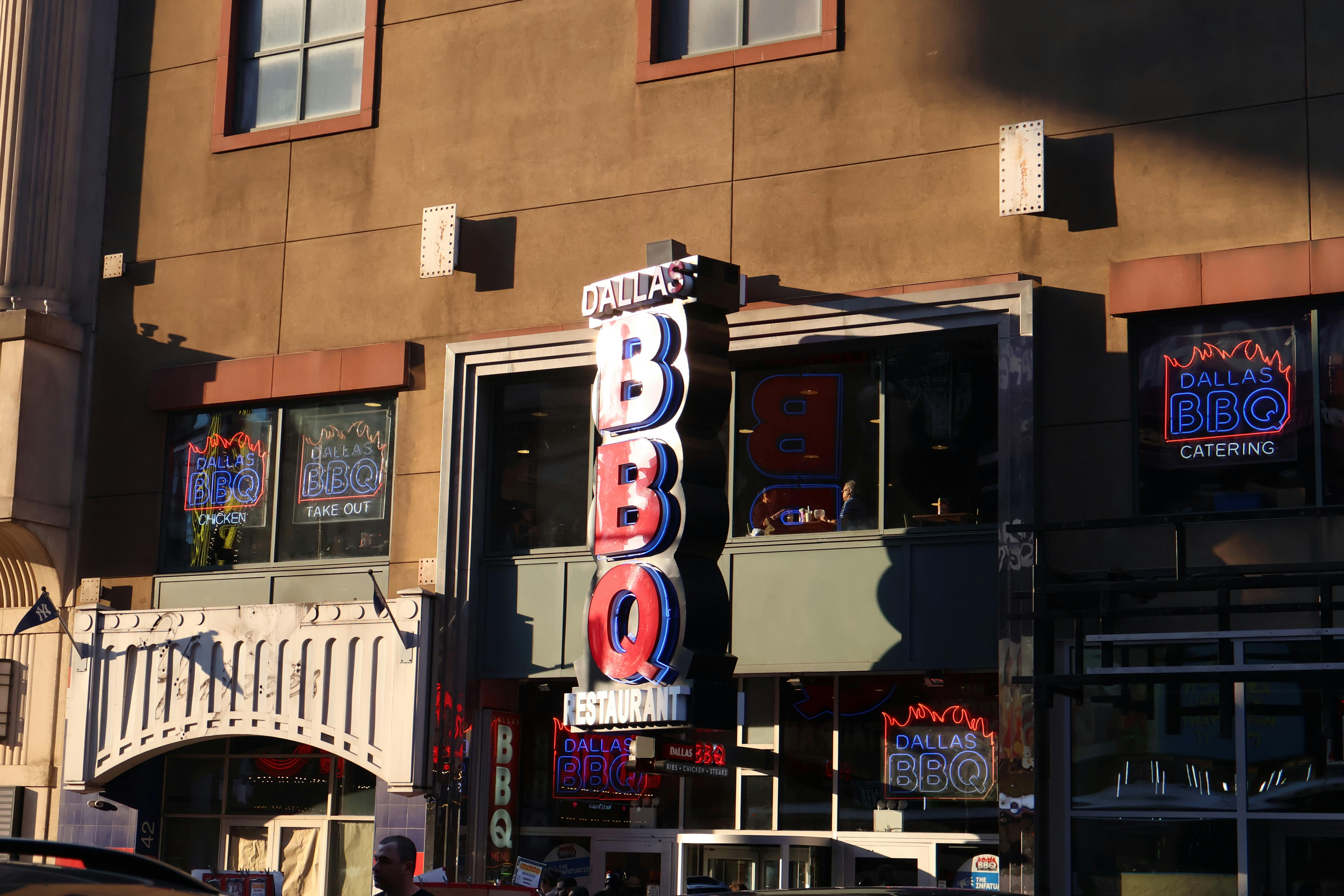 Gratis Insegna al neon del Dallas BBQ Restaurant illuminata in un ambiente urbano al tramonto. Foto a disposizione