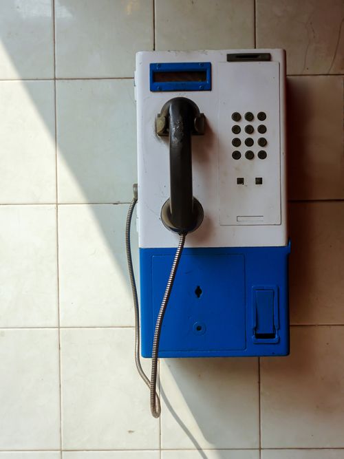 Free A vintage blue and white payphone on a tiled wall with dramatic shadow contrast in Jakarta, Indonesia. Stock Photo