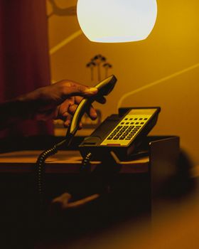 A hand picks up a telephone handset in a warmly lit room, creating a moody ambiance.
