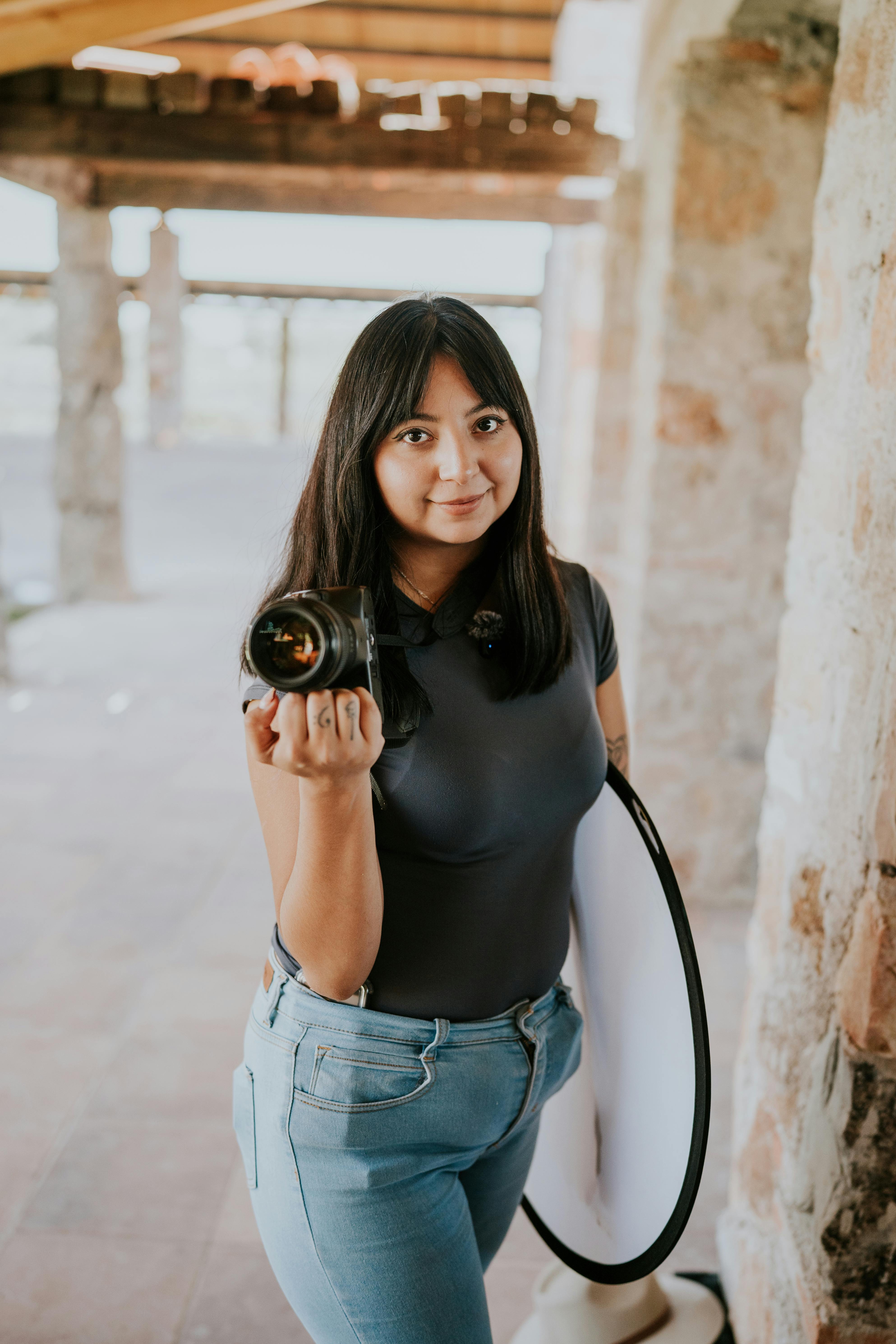 Young female photographer holding a camera and reflector in a rustic setting.