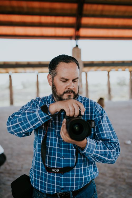 Free A male photographer in a plaid shirt adjusting his camera in an outdoor setting. Stock Photo