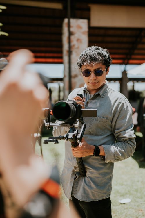 Free A male cinematographer using a camera stabilizer outdoors on a sunny day, focused on his subject. Stock Photo