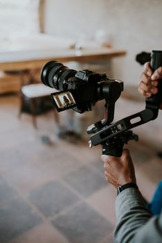 Close-up of hands operating a DSLR camera mounted on a stabilizer rig in an indoor setting.