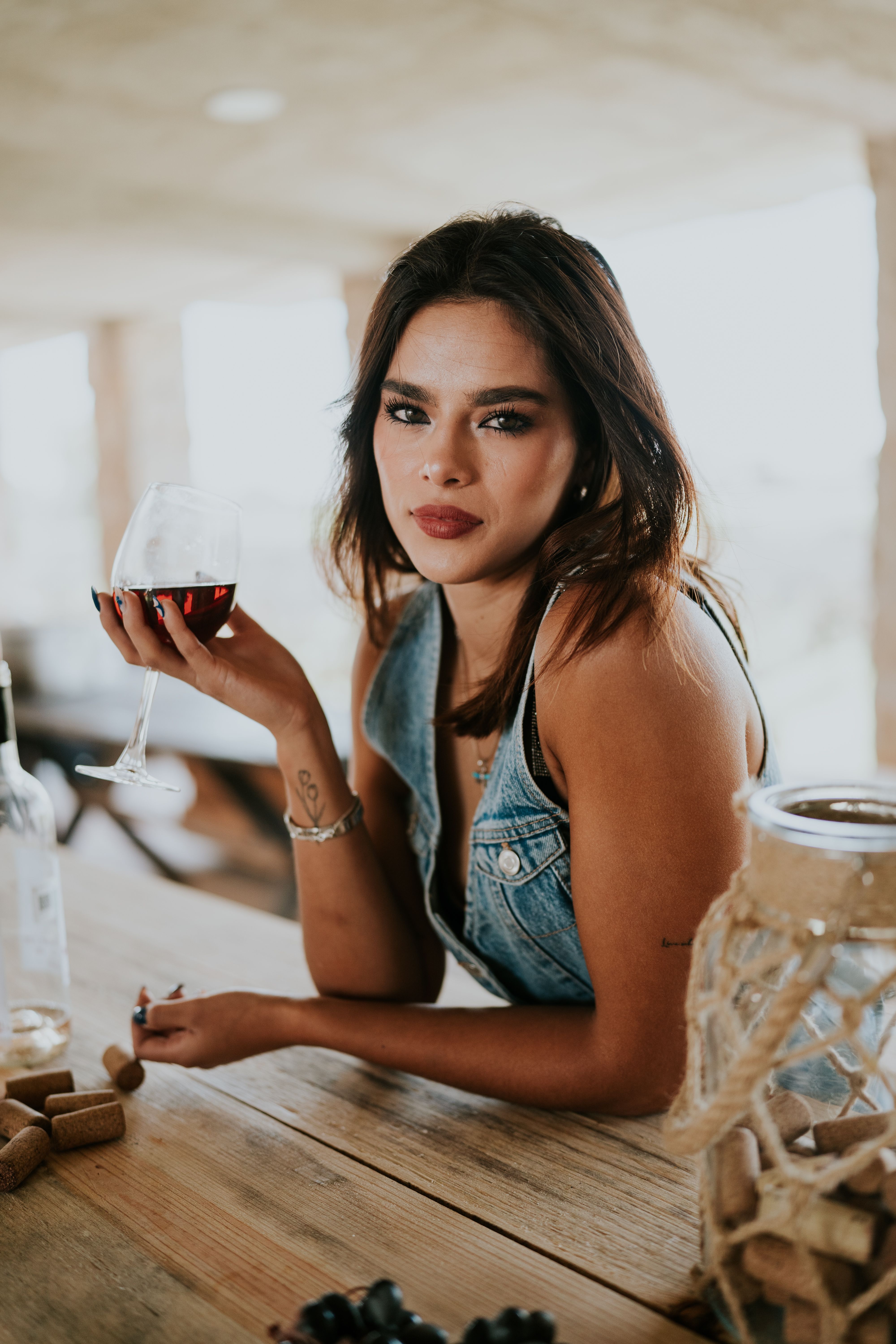 Sophisticated woman savoring wine in a rustic vineyard, wearing a stylish denim vest.