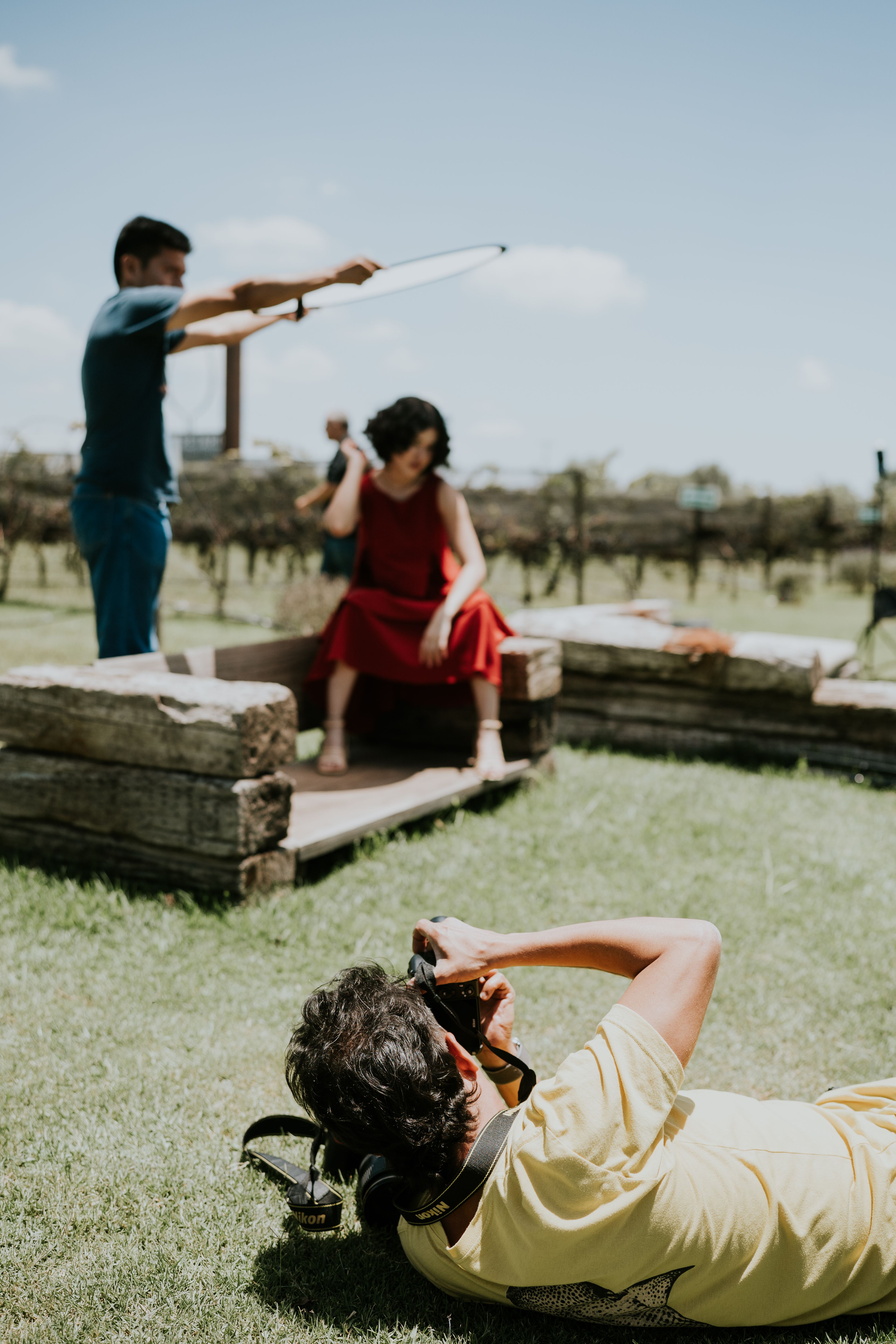 A photographer captures a model in a red dress during an outdoor vineyard photo session.