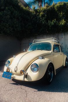 Vintage cream Volkswagen Beetle parked in a sunlit driveway, showcasing nostalgic charm.