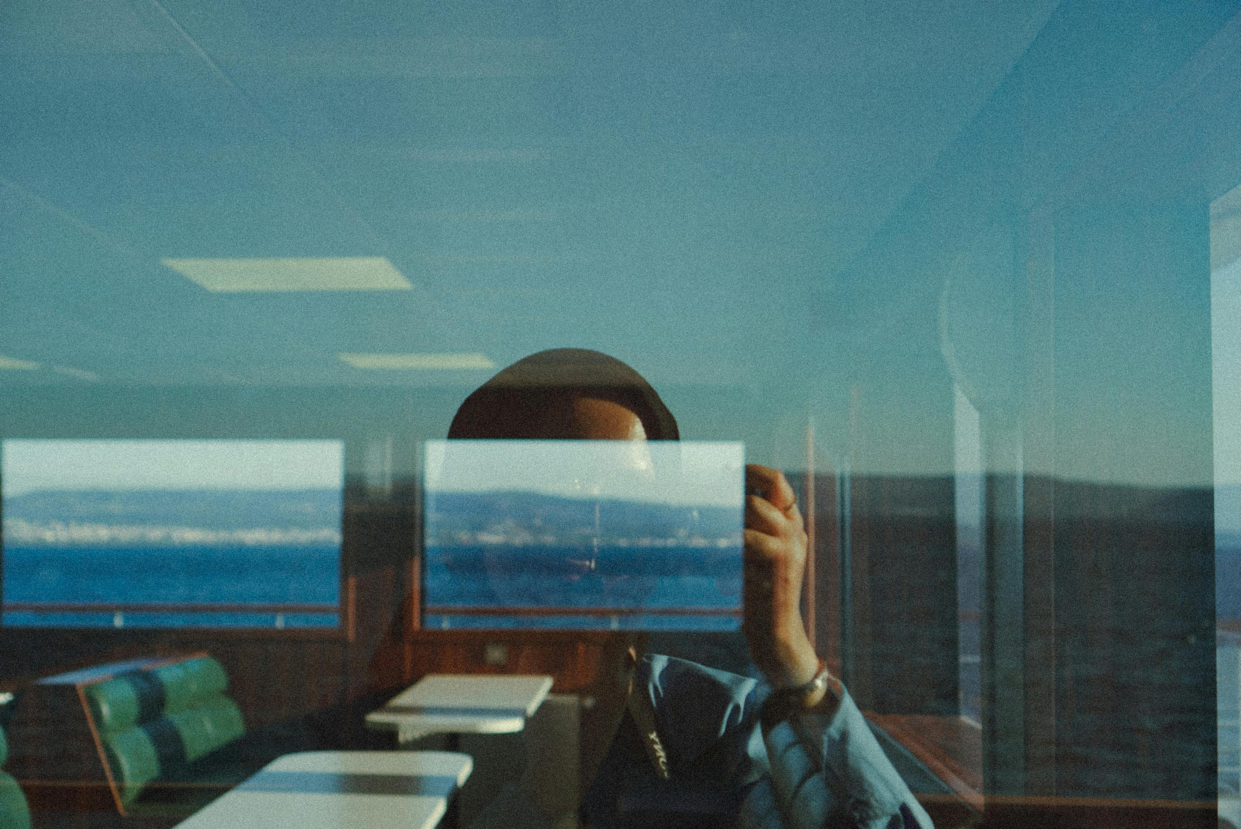 Artistic reflection in a window with ocean in background, capturing a serene travel moment.