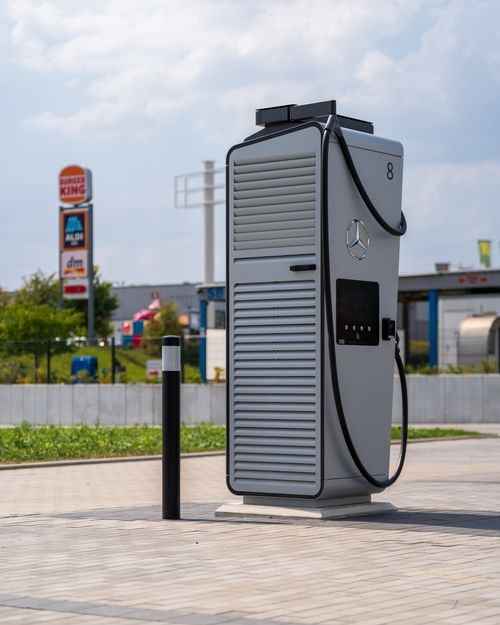 Free Electric vehicle charging station at a commercial area with visible fast-food and retail signs under a cloudy sky. Stock Photo