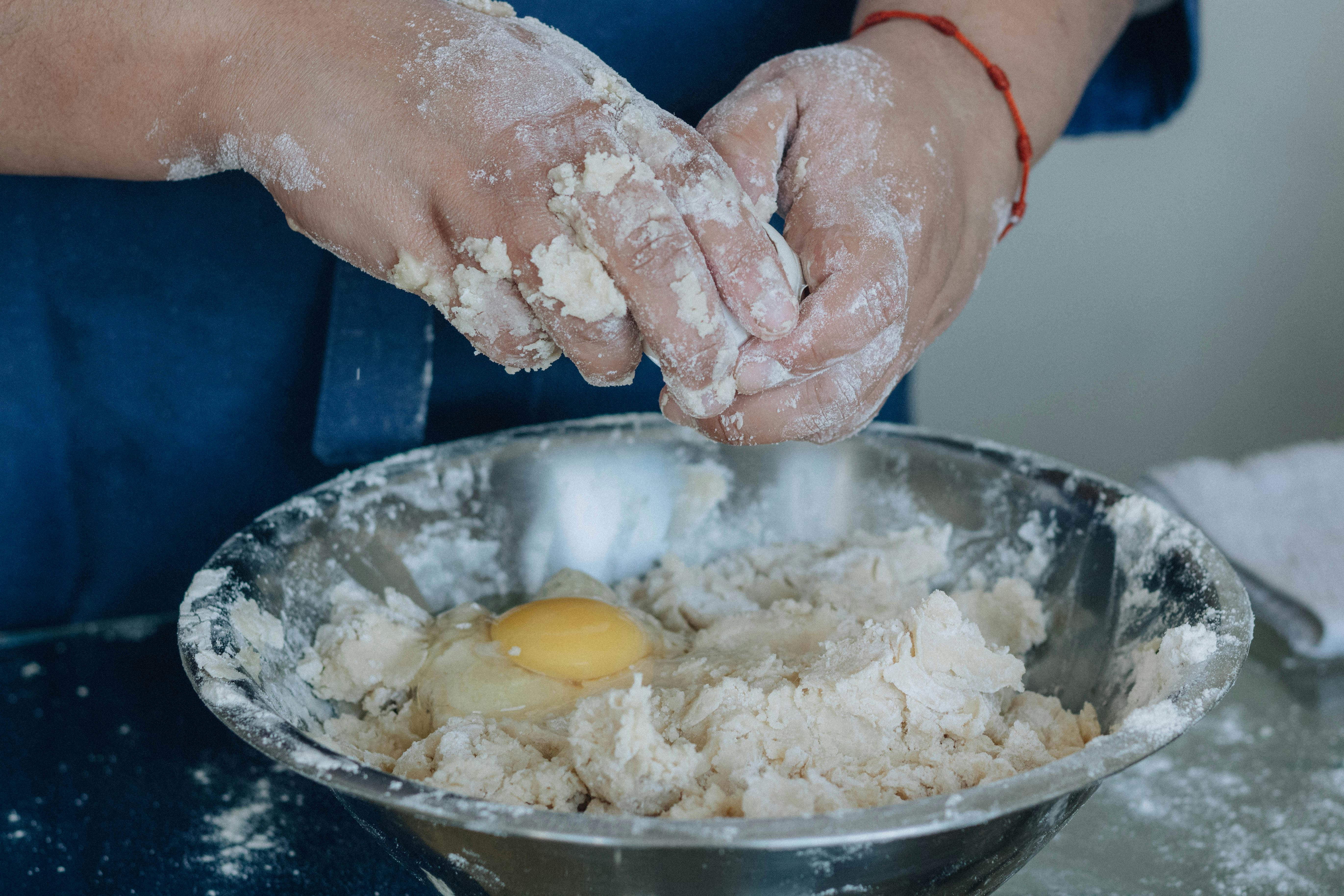 Hands kneading dough with an egg in a bowl, capturing the baking process.