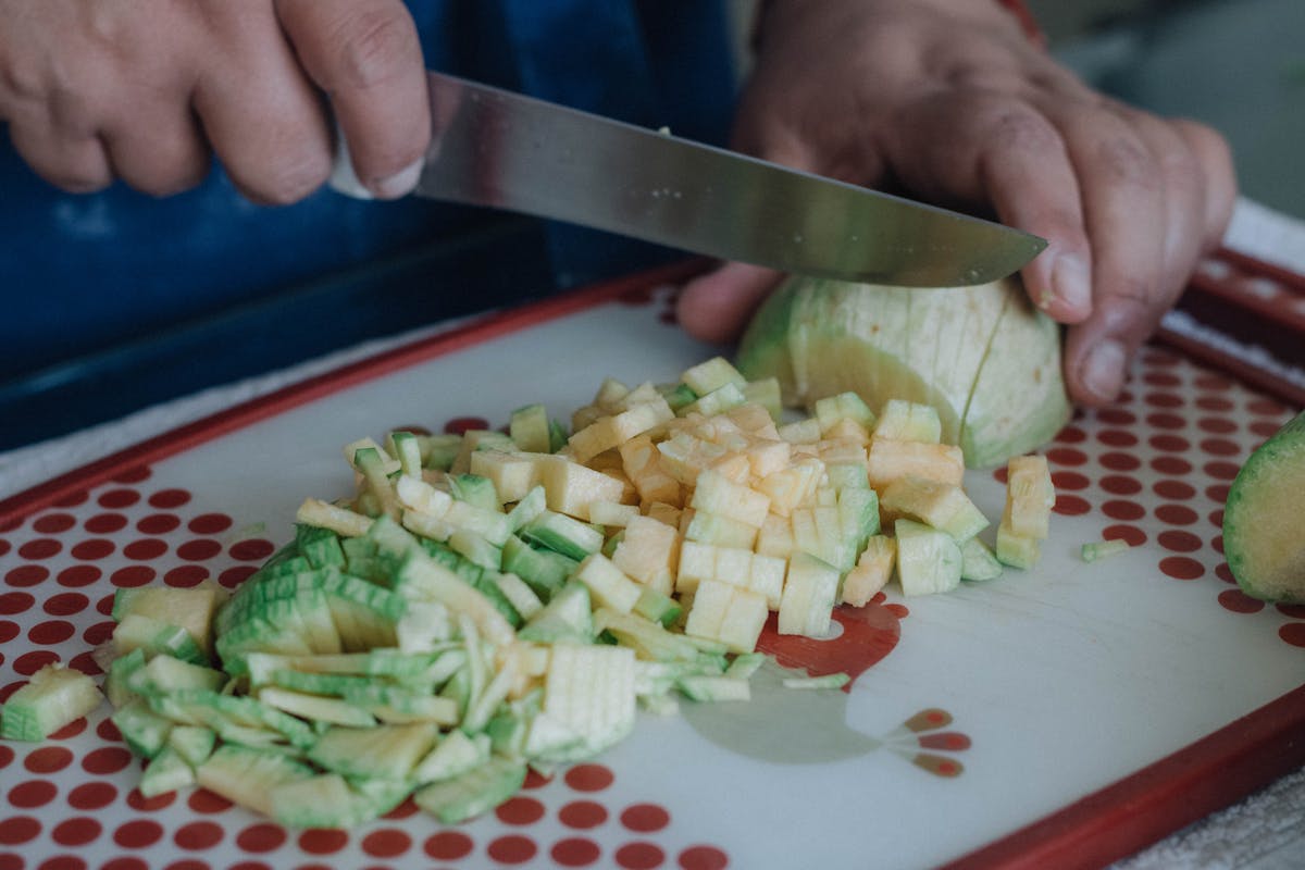 Primo piano di mani che tagliano zucchine su tagliere