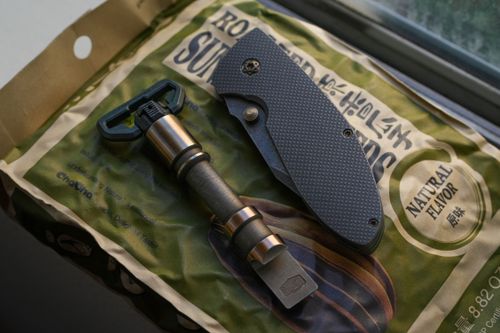 Free Close-up of a folding knife and a tactical tool on a snack packet by a window. Stock Photo