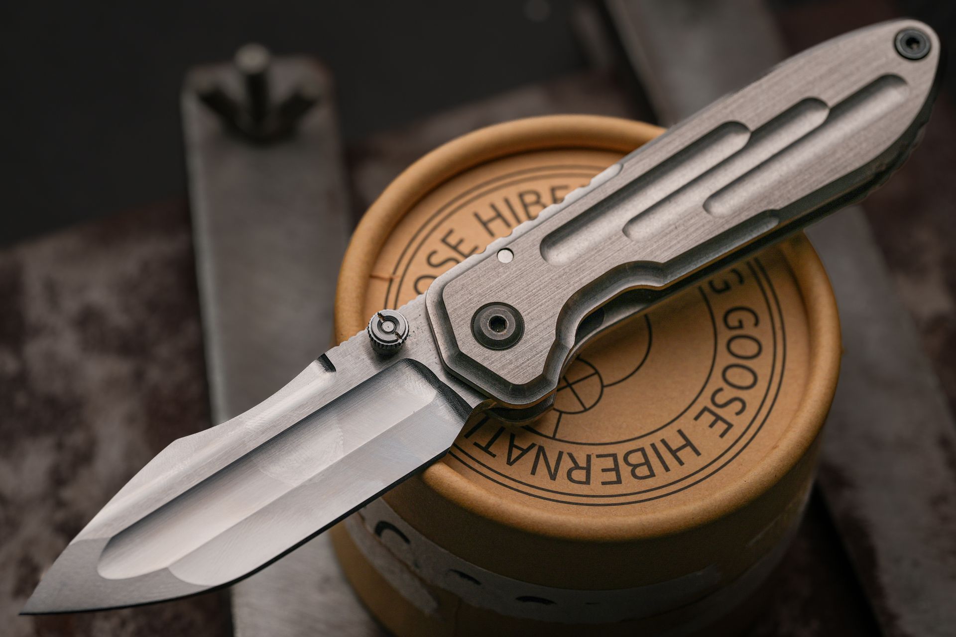 Close-up of a titanium folding knife on a cylindrical box. Ideal for EDC enthusiasts.