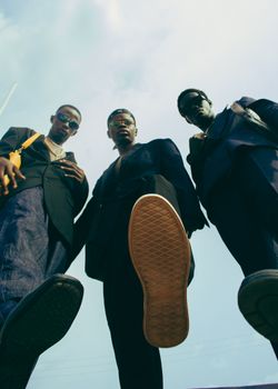 Three stylish men in fashionable suits pose confidently outdoors. Low angle shot.